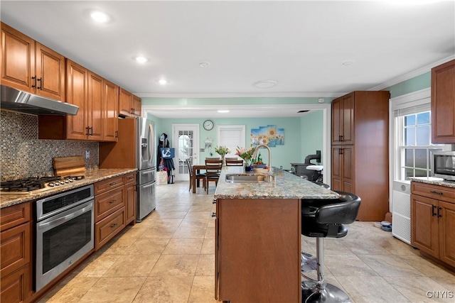 kitchen featuring sink, a kitchen breakfast bar, stainless steel appliances, a kitchen island with sink, and backsplash