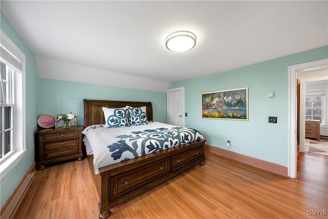 bedroom featuring light wood-type flooring, a baseboard radiator, and vaulted ceiling