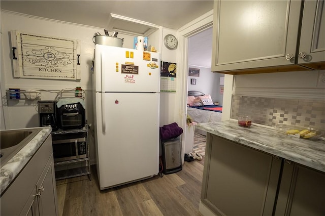 kitchen featuring gray cabinets, decorative backsplash, white refrigerator, light stone countertops, and dark wood-type flooring