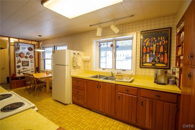 kitchen with hanging light fixtures, sink, track lighting, and white appliances