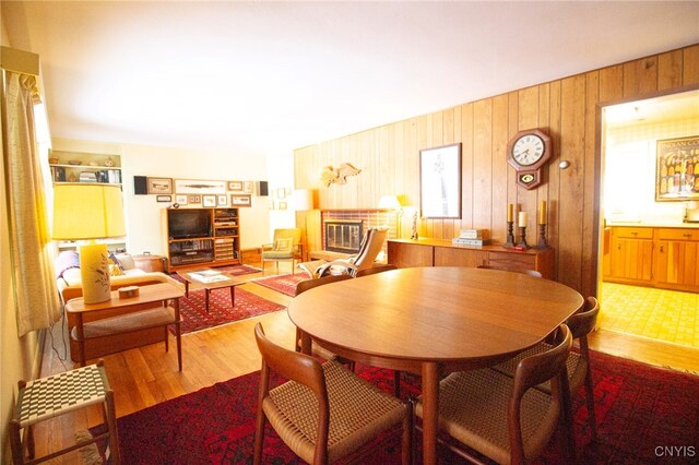 dining area with built in shelves, wood-type flooring, a brick fireplace, and wood walls