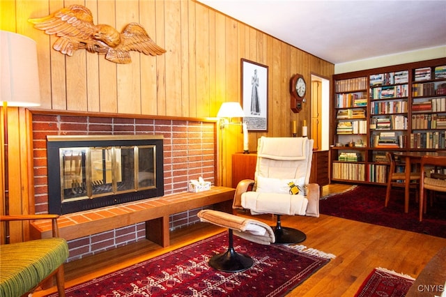 sitting room featuring a brick fireplace, wood-type flooring, and wood walls