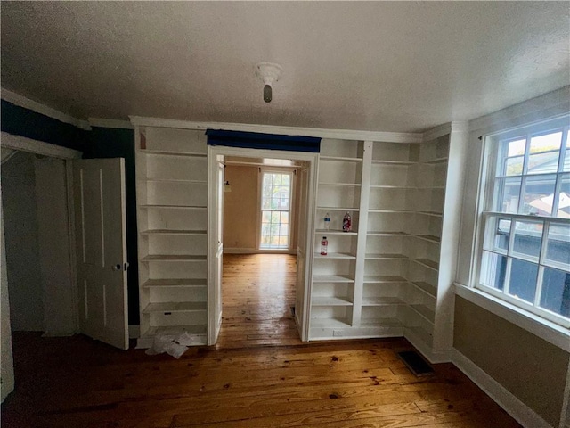 unfurnished room with built in shelves, wood-type flooring, ornamental molding, and a healthy amount of sunlight