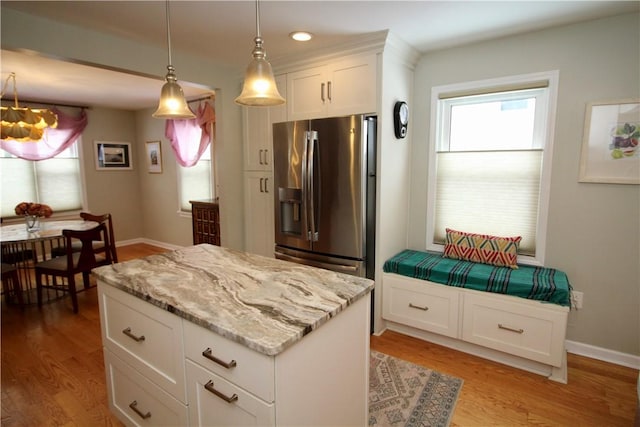 kitchen featuring light stone counters, stainless steel fridge with ice dispenser, white cabinets, and a kitchen island