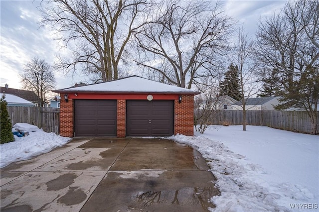 snow covered garage with a garage and fence