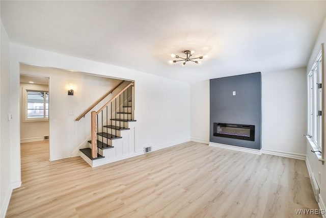 unfurnished living room with an inviting chandelier and light hardwood / wood-style flooring