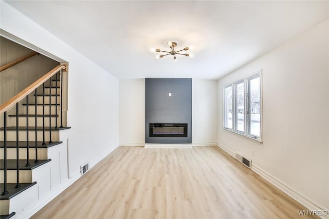 unfurnished living room with an inviting chandelier and light hardwood / wood-style flooring