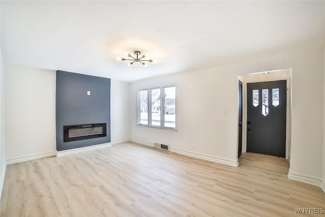 unfurnished living room featuring an inviting chandelier and light hardwood / wood-style flooring