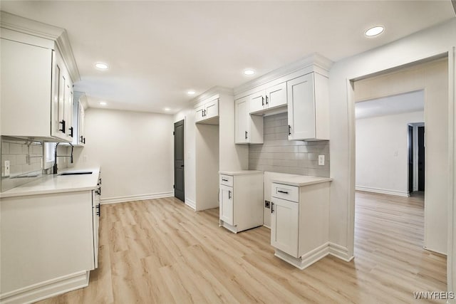 kitchen featuring sink, backsplash, light hardwood / wood-style floors, and white cabinets