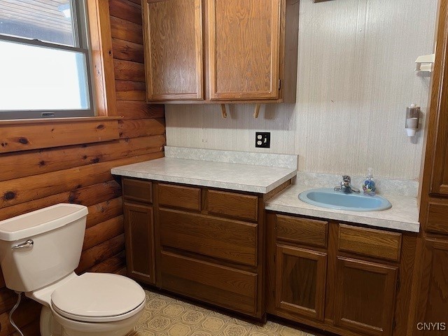 bathroom with toilet, vanity, and log walls