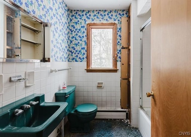 bathroom featuring a wainscoted wall, a baseboard heating unit, combined bath / shower with glass door, a sink, and wallpapered walls