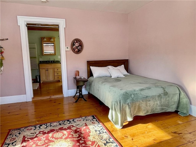 bedroom with connected bathroom, hardwood / wood-style floors, and sink