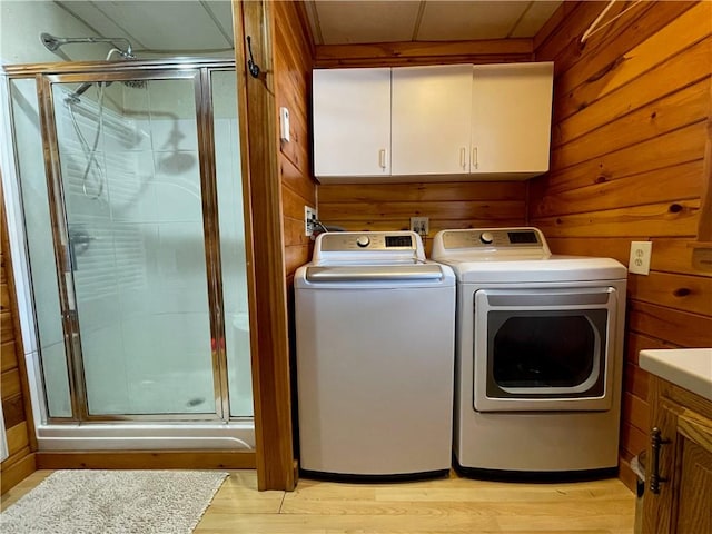 laundry room featuring cabinets, separate washer and dryer, light hardwood / wood-style floors, and wood walls