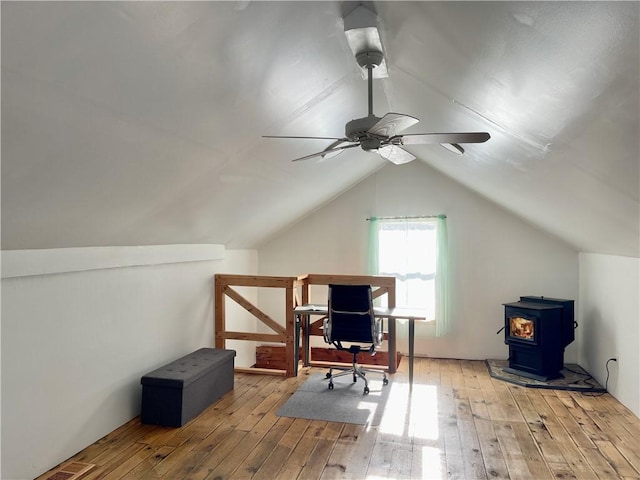 home office featuring vaulted ceiling, ceiling fan, light hardwood / wood-style floors, and a wood stove