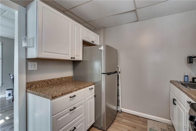 kitchen with light hardwood / wood-style flooring, a paneled ceiling, stainless steel fridge, and white cabinets