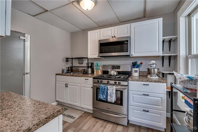 kitchen with stainless steel appliances, a paneled ceiling, white cabinets, and light hardwood / wood-style floors