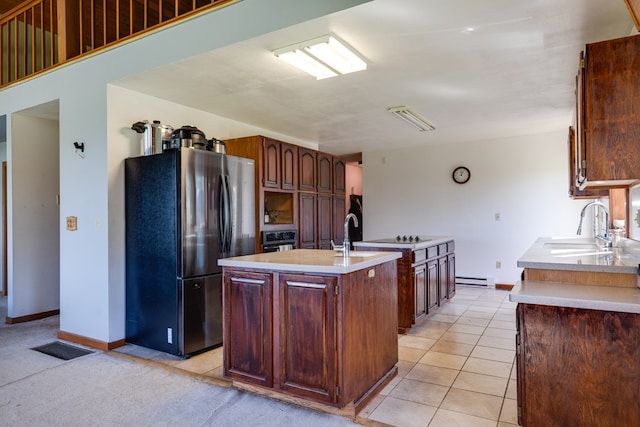 kitchen featuring sink, light tile patterned floors, a baseboard heating unit, black appliances, and a center island with sink