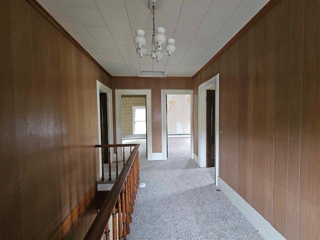 hall with ornamental molding, light carpet, a chandelier, and wood walls