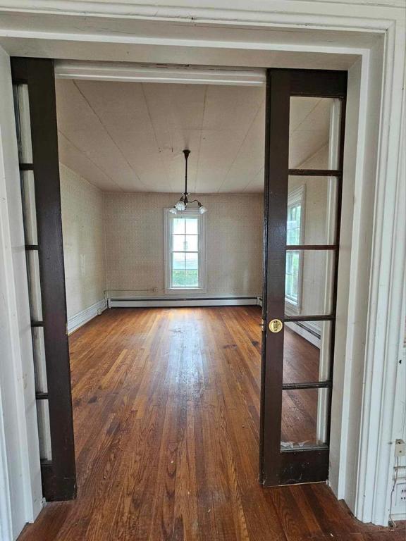 unfurnished dining area featuring hardwood / wood-style flooring, a baseboard radiator, and french doors