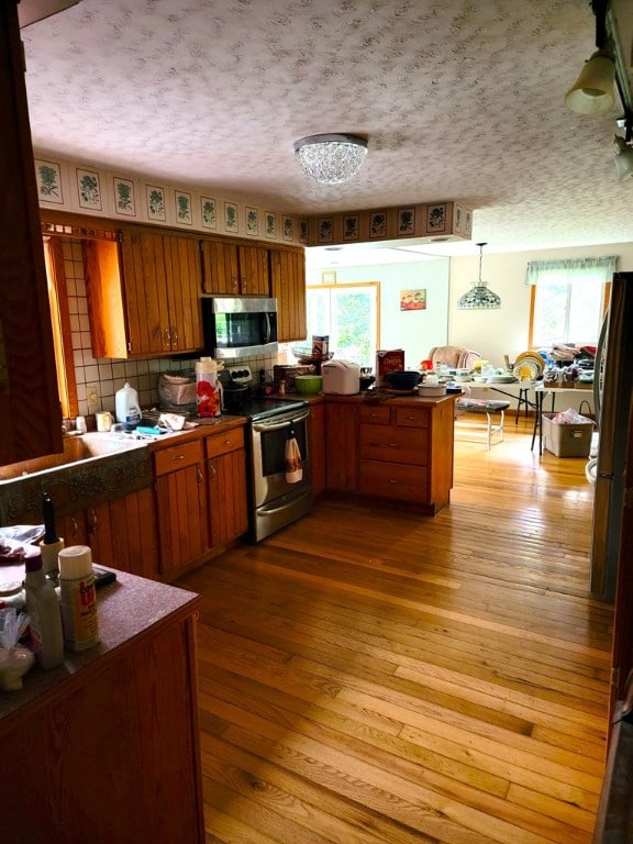 kitchen featuring stainless steel appliances, a wealth of natural light, light hardwood / wood-style floors, decorative light fixtures, and kitchen peninsula