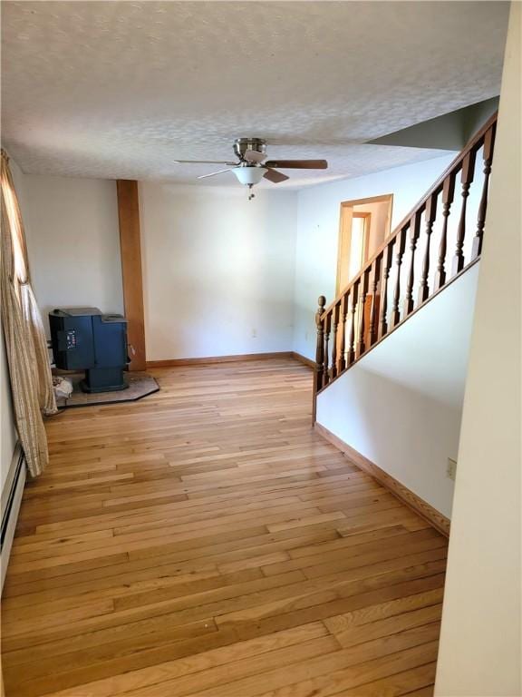 3530 Coats Rd, Hector, NY 14818 - unfurnished living room featuring a ceiling fan, a textured ceiling, baseboards, light wood-style flooring, and a wood stove
