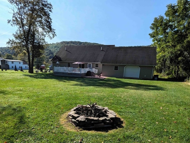 rear view of house featuring a wooden deck, a garage, a lawn, and an outdoor fire pit