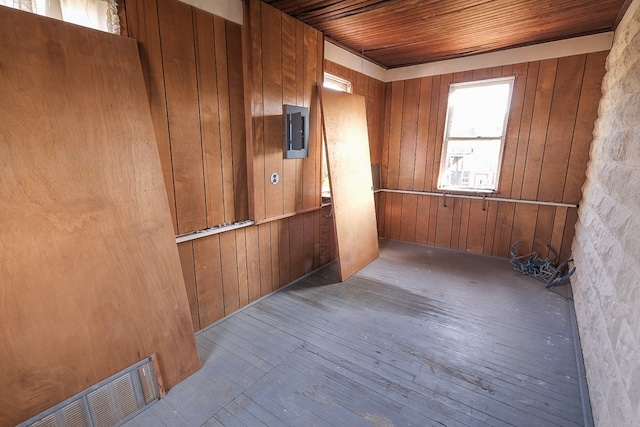 empty room with wood walls, electric panel, light hardwood / wood-style floors, and wooden ceiling