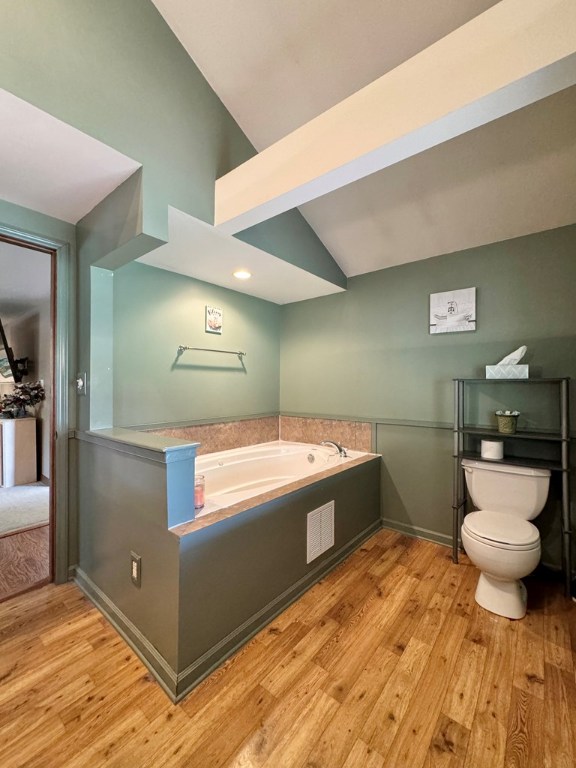 bathroom with a tub to relax in, vaulted ceiling, toilet, and wood-type flooring