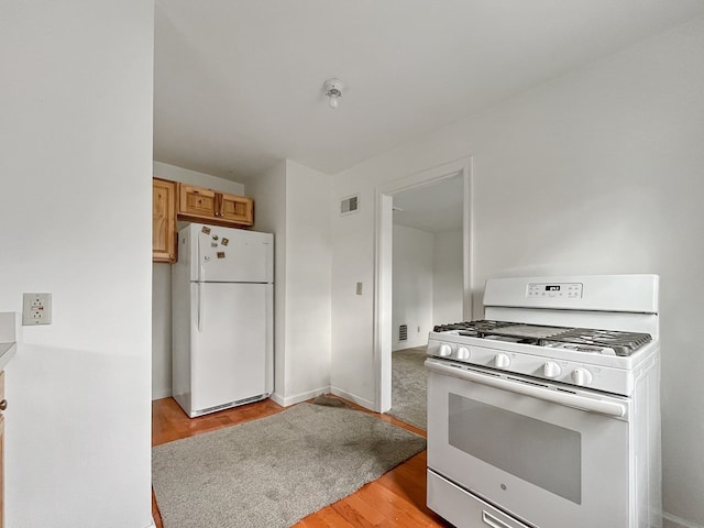 kitchen with light brown cabinets, white appliances, and light hardwood / wood-style flooring