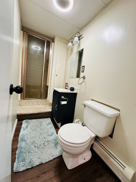 bathroom featuring hardwood / wood-style flooring, baseboard heating, vanity, toilet, and walk in shower