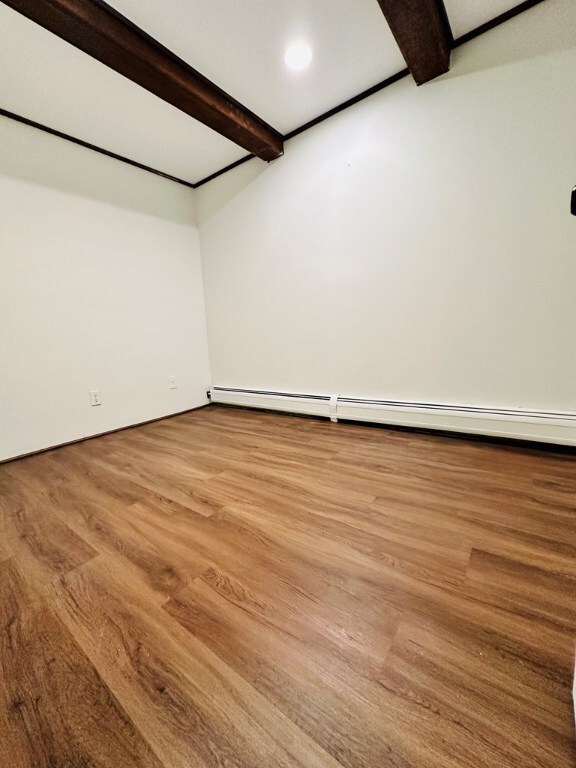 empty room featuring baseboard heating, beam ceiling, and light wood-type flooring