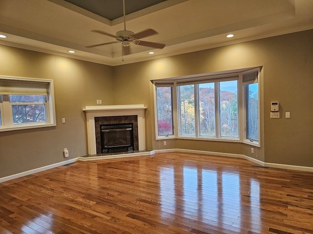 unfurnished living room featuring crown molding, wood-type flooring, a raised ceiling, ceiling fan, and a high end fireplace