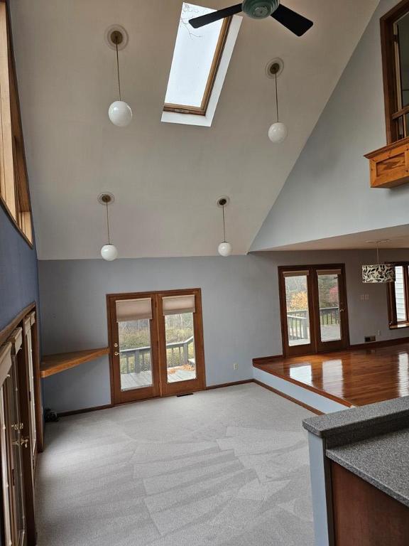 unfurnished living room with ceiling fan, a skylight, high vaulted ceiling, light carpet, and french doors