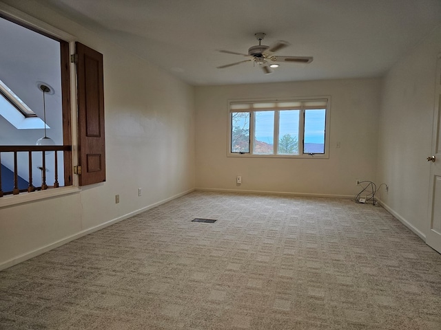 carpeted empty room featuring ceiling fan and a skylight