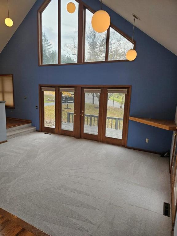 unfurnished living room featuring a healthy amount of sunlight, carpet flooring, and high vaulted ceiling