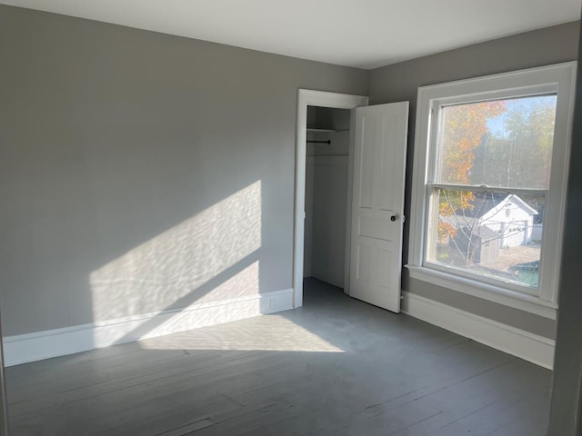 unfurnished bedroom with a closet, dark hardwood / wood-style floors, and multiple windows