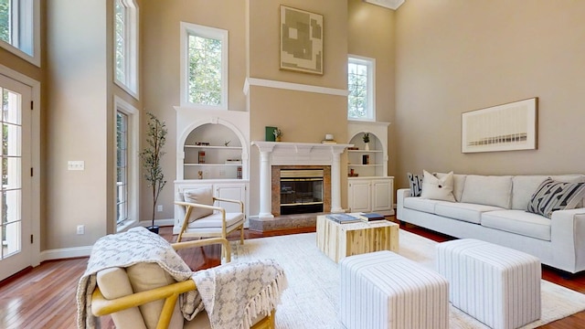 living room featuring a high ceiling, wood-type flooring, a fireplace, and built in shelves