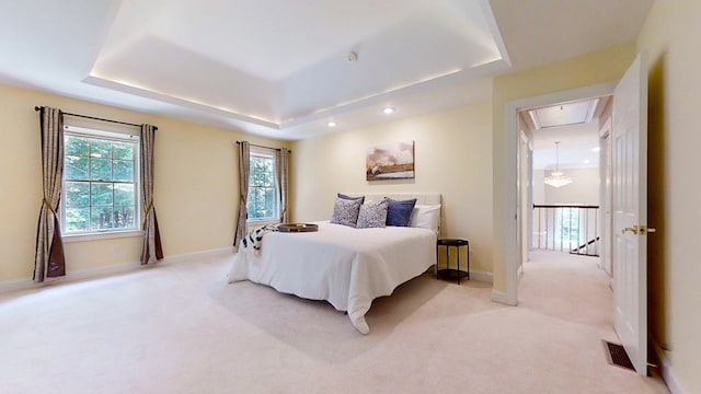 bedroom with light carpet, multiple windows, and a raised ceiling