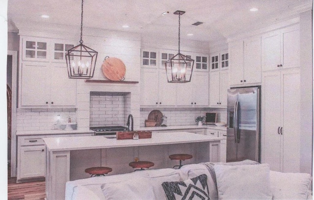 kitchen with white cabinetry, a breakfast bar, a center island with sink, and stainless steel fridge