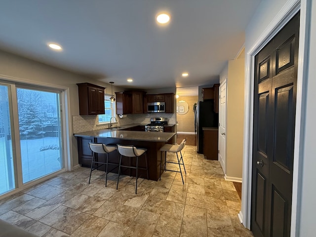 kitchen featuring hanging light fixtures, appliances with stainless steel finishes, a kitchen breakfast bar, kitchen peninsula, and backsplash