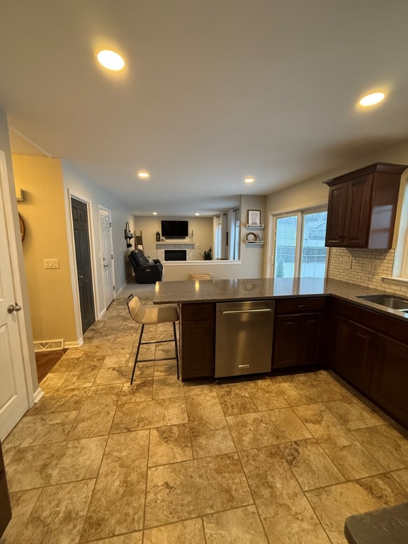 kitchen with a kitchen breakfast bar, dark brown cabinetry, tasteful backsplash, stainless steel dishwasher, and kitchen peninsula