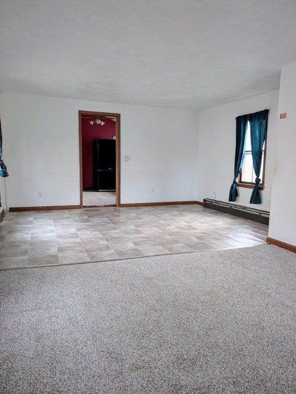 empty room featuring light colored carpet and a baseboard heating unit