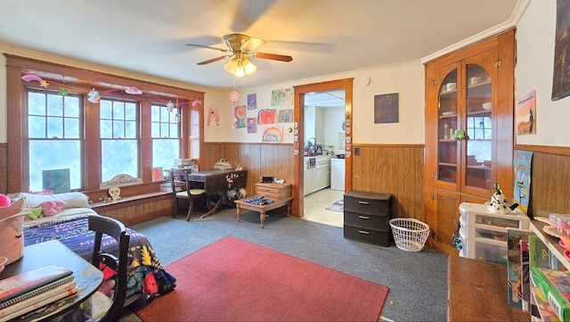 carpeted home office featuring crown molding, ceiling fan, plenty of natural light, and wooden walls