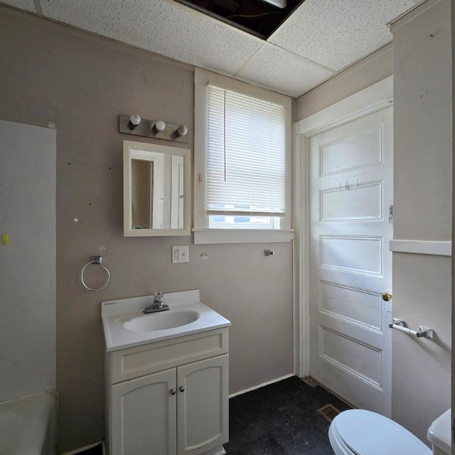 bathroom with vanity, toilet, a bathtub, and a drop ceiling