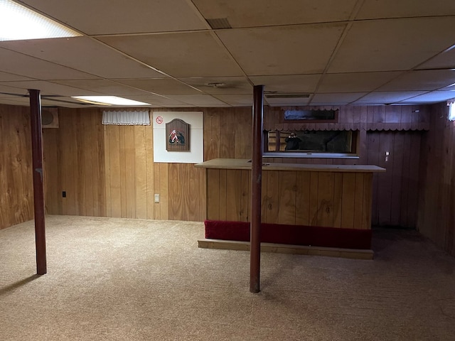 finished below grade area with a bar, carpet, a paneled ceiling, and wooden walls