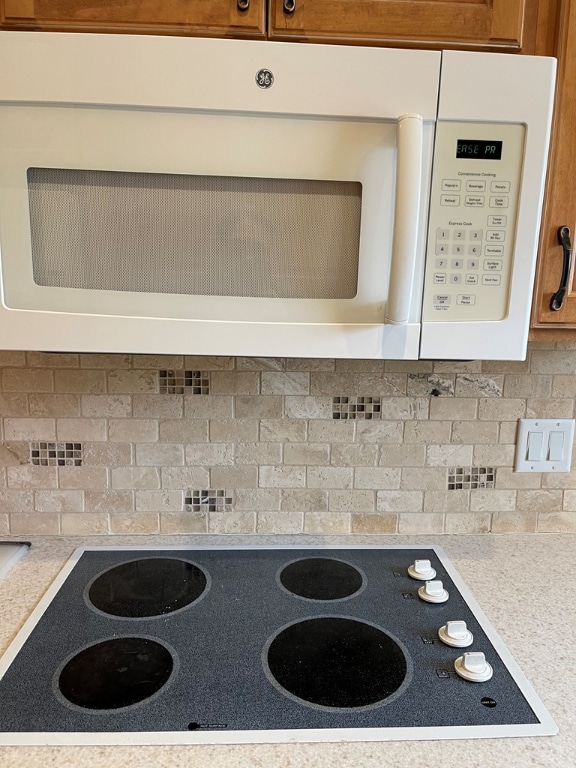 details featuring tasteful backsplash, electric cooktop, white microwave, brown cabinets, and light countertops