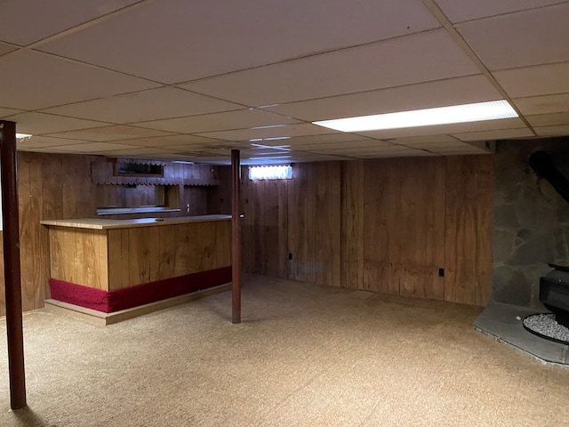 below grade area with a bar, wood walls, a drop ceiling, and a wood stove