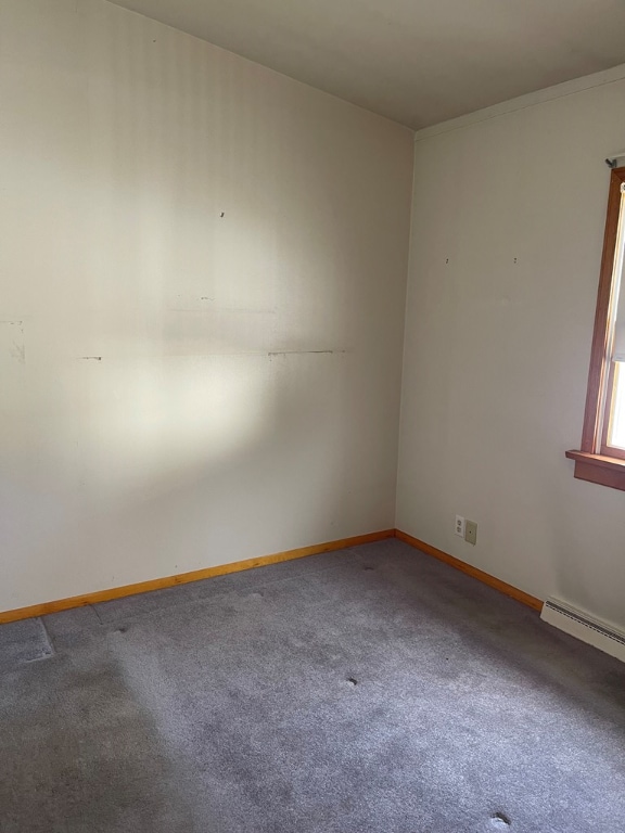 carpeted empty room featuring a baseboard heating unit and baseboards