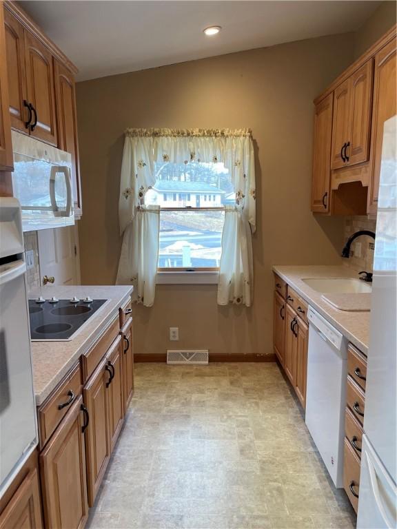 kitchen featuring light countertops, visible vents, brown cabinetry, a sink, and white appliances