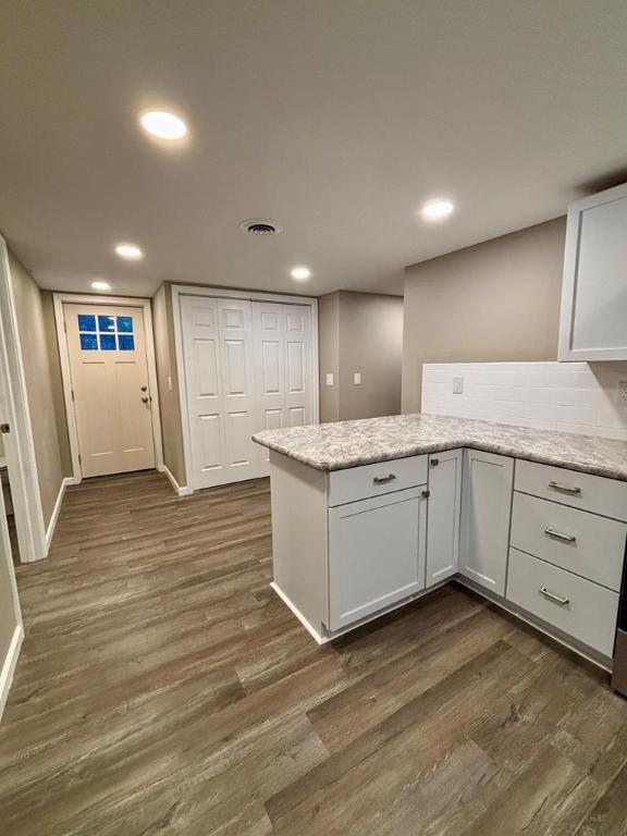 kitchen with white cabinetry, dark hardwood / wood-style floors, light stone countertops, and kitchen peninsula